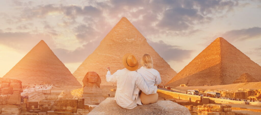 Back view lover couple, Tourists woman and man with hat background Sphinx and pyramid of Egyptian Giza, sunset Cairo, Egypt. Is It Safe To Travel to Egypt Now