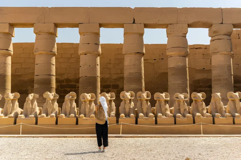 Female tourist walking at the Karnak Temple in Luxor among alley of sphinxes in Thebes