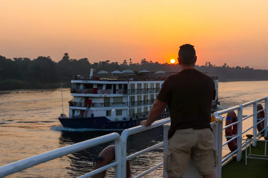 Man on his back leaning over the white railing of cruise in the Nile river looking at sunset