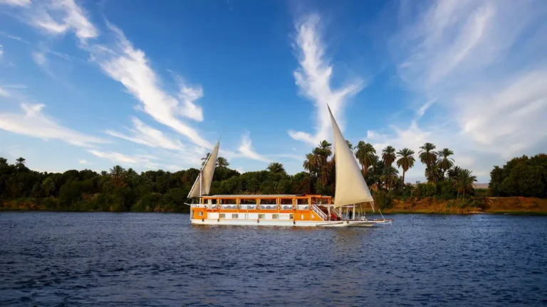 Side view of Amoura Dahabiya sailing past palm trees on the Nile